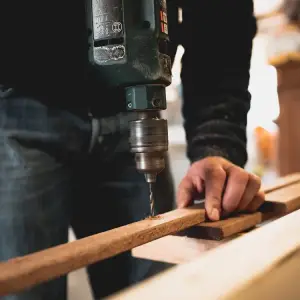 a man drilling and holding a piece of wood