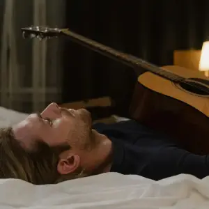 a man lying on his bed with his guitar