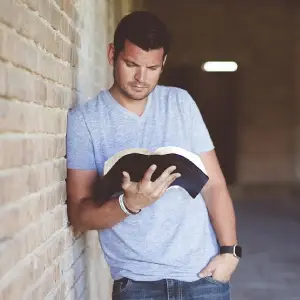 a man reading a book while leaning on a wall
