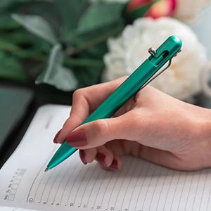 A woman's hand holding a green Bastion pen while writing on paper